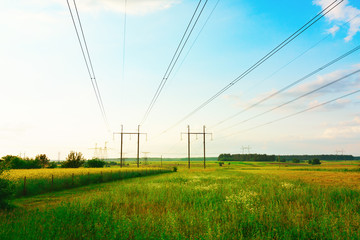 High voltage steel electricity transmission lines pylons of a power line on a green field. Scenery rural summer landscape. Supply, distribution, transmitting energy concept.