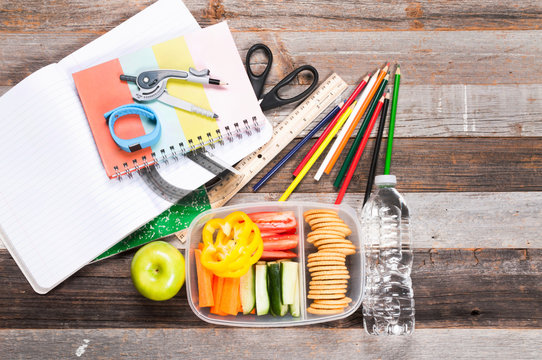 School supplies and lunch on wooden background.