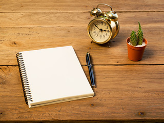 Blank notebook with vintage alarm clock and black pen and cactus on wood table