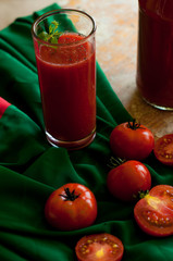Glass and bottle of tomato juice with vegetables and green napkin on wooden background