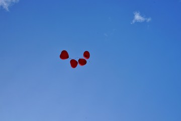 Heart shaped red balloons flying loose on a blue sky 