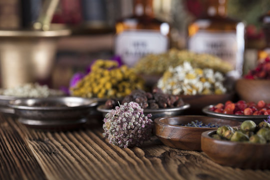 Alternative medicine. Wooden table, shallow depth of focus. Mortar, berries, flowers and herbs assorted in bowls. 