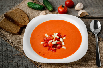 Gazpacho tomato soup in a white bowl spoon on a towel on the background of wooden boards