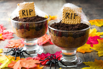 Funny Halloween chocolate mousse with tomb cookie on wooden table
