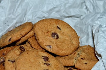 A pile of freshly baked homemade chocolate chip cookies on crumpled parchment paper. Close-up of a delicious comfort food dessert.