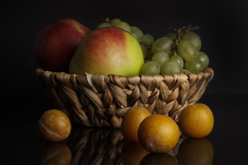 Assorted fruits. Apple, plum and grapes in a basket on a black background
