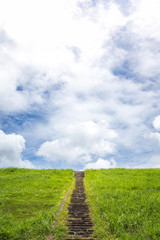 Stone steps on the grass under blue sky with clouds.