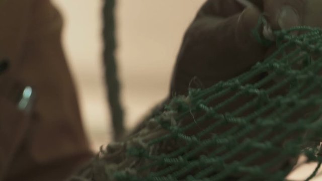 Close up of a man's hands repairing fishing net indoor in Sicily