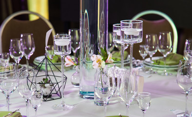 Closeup of beautifully decorated by candles and flowers festive table ready for guests. Elegant setup for wedding or other holiday celebration in restaurant. Horizontal color image.