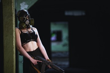 Beautiful, young girl post apocalypse girl stand in abandoned factory with gas mask and machine gun