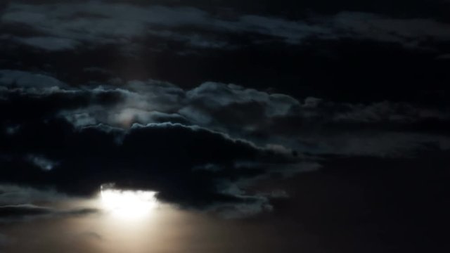 Time-lapse. Full moon close-up rises through the clouds in the dark.