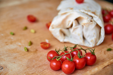 Vegetarian burrito with vegetables on blurred background. On foreground small cherry tomatoes on brown wooden background close up. Side view