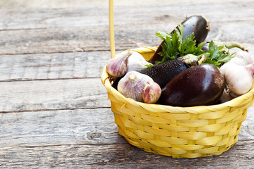 A wicker basket of vegetables eggplant garlic greens on wooden concrete background on the street. Selective focus. Copy space.