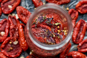 Jar with many dried red tomatoes and spices on a dark surface close up. Dried tomatoes texture blurred background. Top view