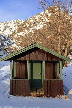 Brown-green painted small wooden cottage. Tinddalstinden-Stottlikollen-Tindstinden mounts background. A-Moskenes-Lofoten-Nordland-Norway. 0313