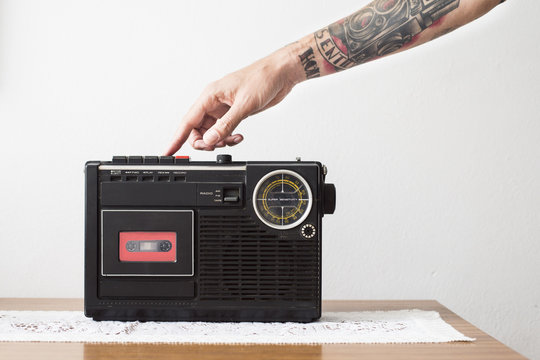 Tattooed arm pushing play button of tape recorder