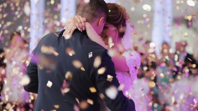 Young beautiful bride and groom dancing first dance at the wedding party shrouded by confetti. Wedding bouquet. Feel happy.