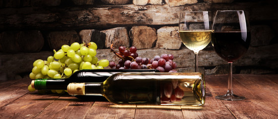 Rode wijnfles en witte wijn met druiven en glazen op houten achtergrond
