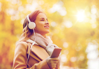woman with smartphone and earphones in autumn park