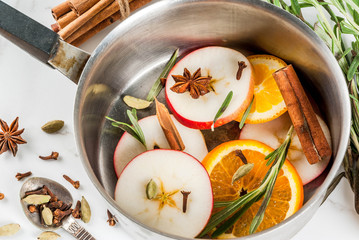 Traditional winter and christmas beverage, ingredients for mulled wine hot drink with citrus, apple and spices in aluminum casserole on white marble table. copy space top view