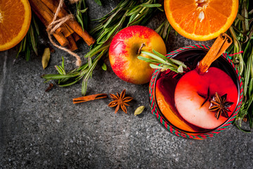 Traditional winter and autumn drinks. Christmas and Thanksgiving Cocktails. Mulled wine with orange, apple, rosemary, cinnamon and spices on a dark stone background, copy space top view