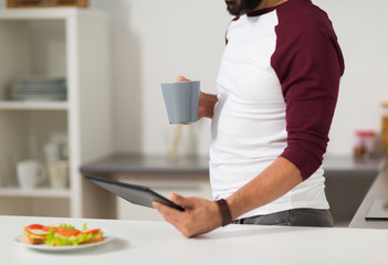 man with tablet pc eating at home kitchen