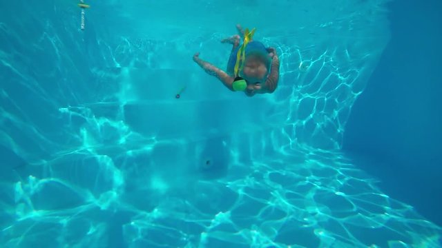 Children's games in the pool.
A little, cute boy sinking in the pool and hunting toys. Underwater shot. Slow motion.