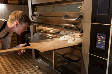 baker putting dough into bread oven at bakery