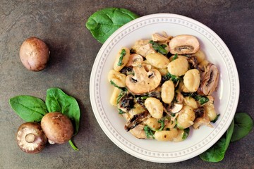 Gnocchi with a mushroom cream sauce, spinach, chicken and sun dried tomatoes, top view on a dark stone background - obrazy, fototapety, plakaty