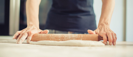 Woman rolling dough on wooden table with wooden rolling pin