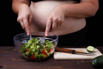 Overweight fat woman mixing a vegetable salad in a bowl. Healthy tasty low-calorie food for weight losing