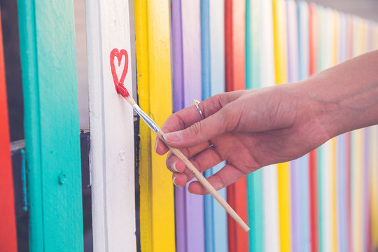 Woman draw heart on colorful fence with painting brush
