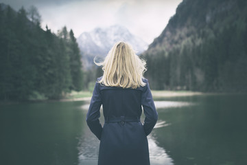 Blonde woman standing backwards and watching magic lake in mountainous country landscape. - Powered by Adobe