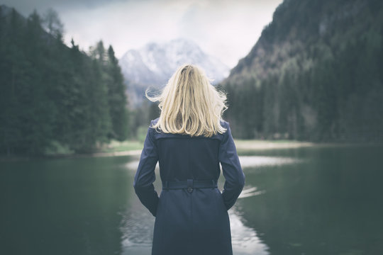 Blonde Woman Standing Backwards And Watching Magic Lake In Mountainous Country Landscape.