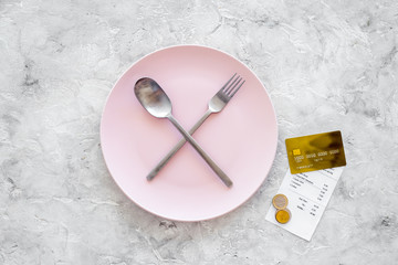 Meal is over. Bill and bank card near plate with crossed spoon and fork on grey stone table top view copyspace