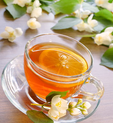 Tea with lemon. Transparent cup with tea and lemon on a wooden table. Branches of flowering jasmine.