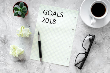 Goals list for 2018. Sheet of paper near pen, glasses and cup of coffee on grey stone background top view mockup