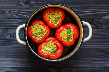 Four red stuffed peppers in a yellow saucepan on dark rustic kitchen table background, top view. Cooking process