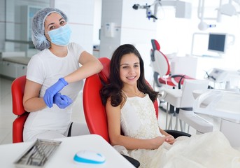 Fototapeta premium Dentist girl treats teeth to baby girl in smart dress in red dental chair
