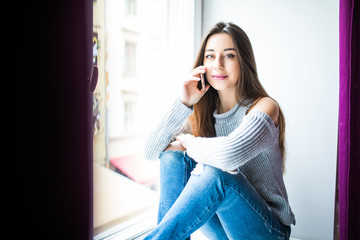 Fototapeta premium Pretty girl with talking by phone sitting on window sill.
