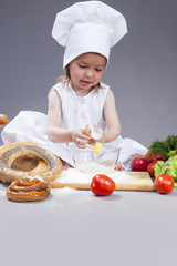 Food Concepts and Ideas. Funny Smiling Little Caucasian Girl In Cook Uniform Making a Mix of Flour, Eggs and Vegetables In Studio Environment.