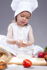 Food Concepts and Ideas. Funny Smiling Little Caucasian Girl In Cook Uniform Making a Mix of Flour, Eggs and Vegetables In Studio Environment.