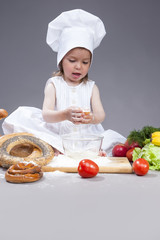 Food Concepts and Ideas. Funny Smiling Little Caucasian Girl In Cook Uniform Making a Mix of Flour, Eggs and Vegetables In Studio Environment.