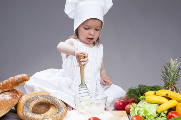 Food Concepts and Ideas. Funny Smiling Little Caucasian Girl In Cook Uniform Making a Mix of Flour, Eggs and Vegetables With Whisk In Studio Environment