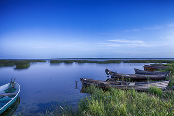 Scenic Destinations. Line of Boats on Water Placed in Belarussian National Park Braslav Lakes at Sunset during Summer Time.