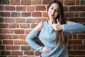 Obraz na płótnie Canvas Beautiful young woman in casual wear with thumbs up, smiling, standing against white brick wall