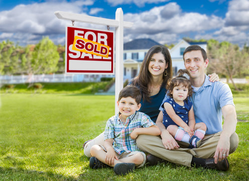 Young Family With Children In Front of Custom Home and Sold For Sale Real Estate Sign.