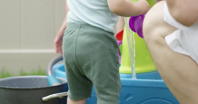 toddler filling dumping bucket of water into kiddy pool - outdoor summer heatwave