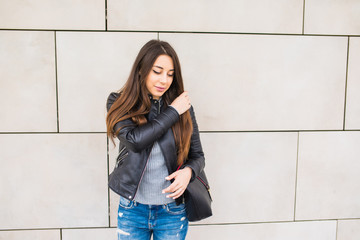 Smiling young girl leaning with bag on building wall