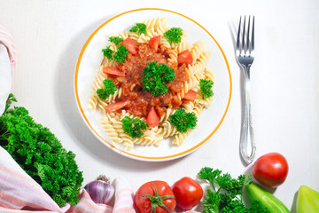 plate of pasta with tomato sauce and fork with ingredients for cooking on white background, top view with copy space